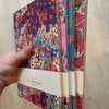 Set of colorful notebooks with floral patterns held by a hand against a neutral background