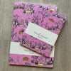 Set of pink patterned notebooks with a card on a wooden surface