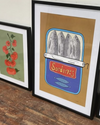 Framed artwork of sardines on a wooden surface with other framed prints.