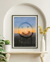 Framed abstract art piece on a wall above a wooden shelf with plants and a vase.