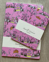 Set of pink patterned notebooks with a card on a wooden surface