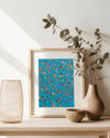 Framed artwork art print with a blue mermaid ocean background and abstract design on a wooden table with decorative items.
